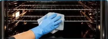 Gloved hand wiping the inside of an oven beneath its metal shelves